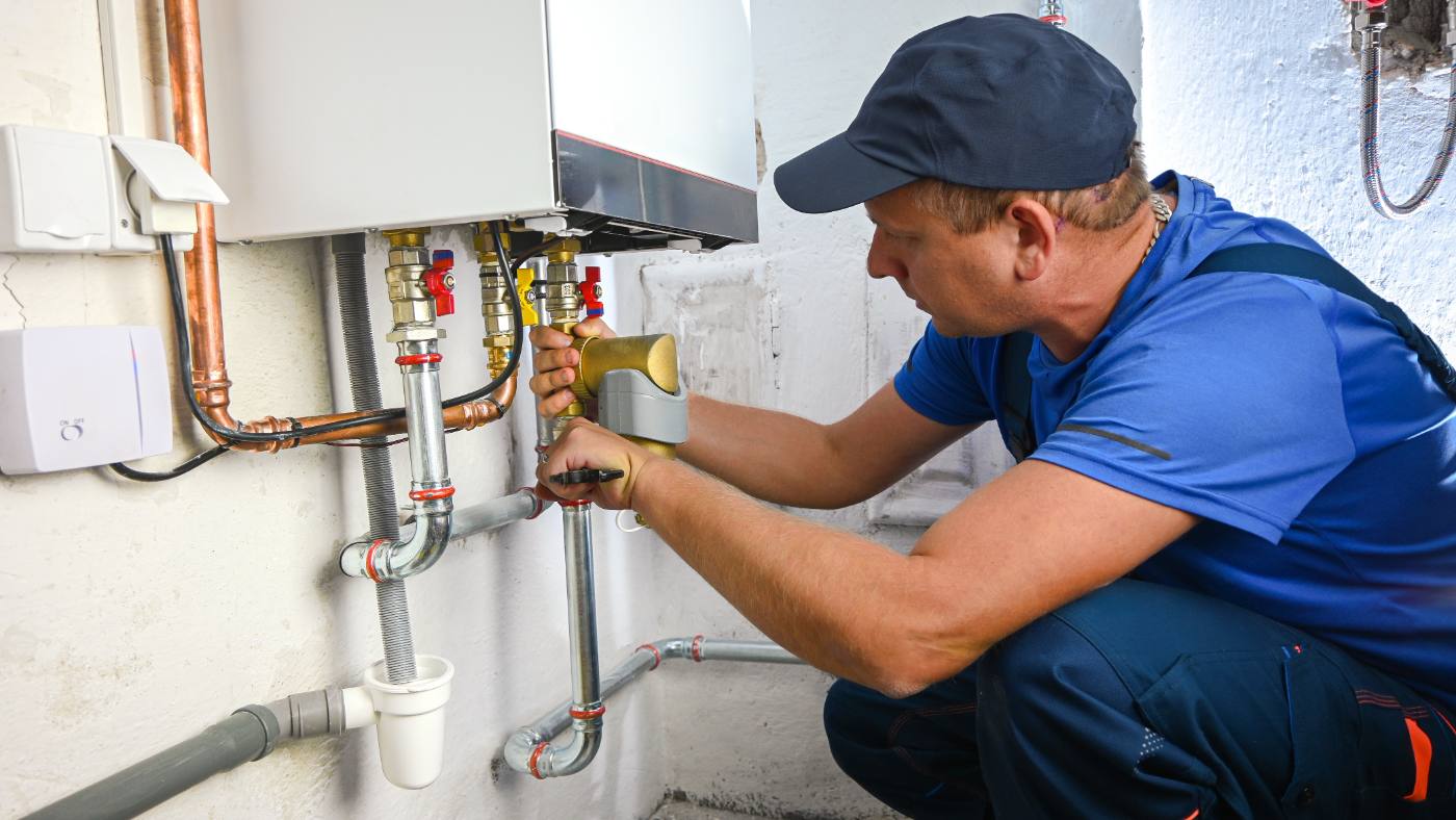 Licensed plumber servicing a tankless water heater and shut-off valves in a Riverside home